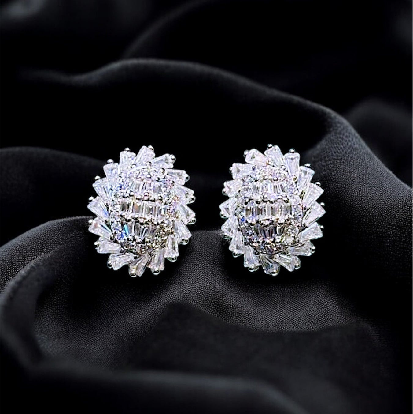 Pair of silver earrings with clear stones on a black fabric background