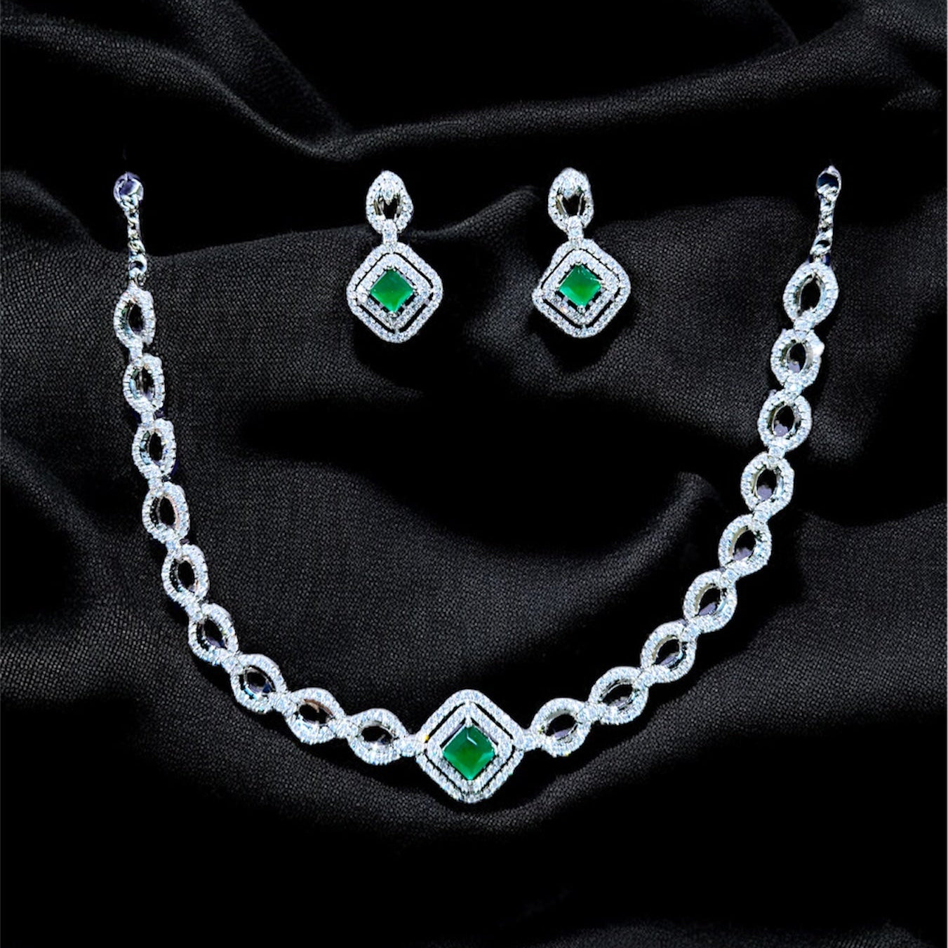 Jewelry set with necklace and earrings featuring green gemstones on a black fabric background