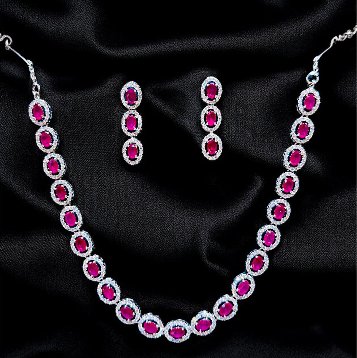 Necklace and earrings with red gemstones on a black satin background