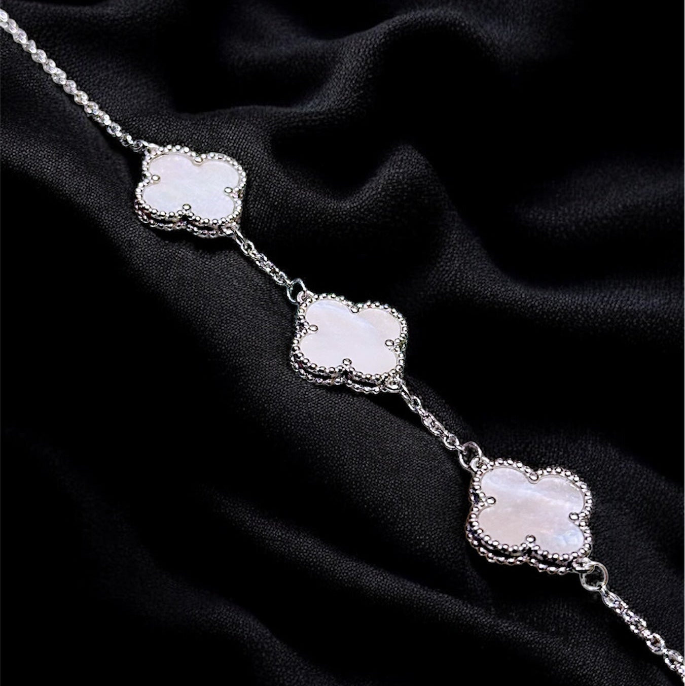 Silver necklace with three floral pendants on a black fabric background