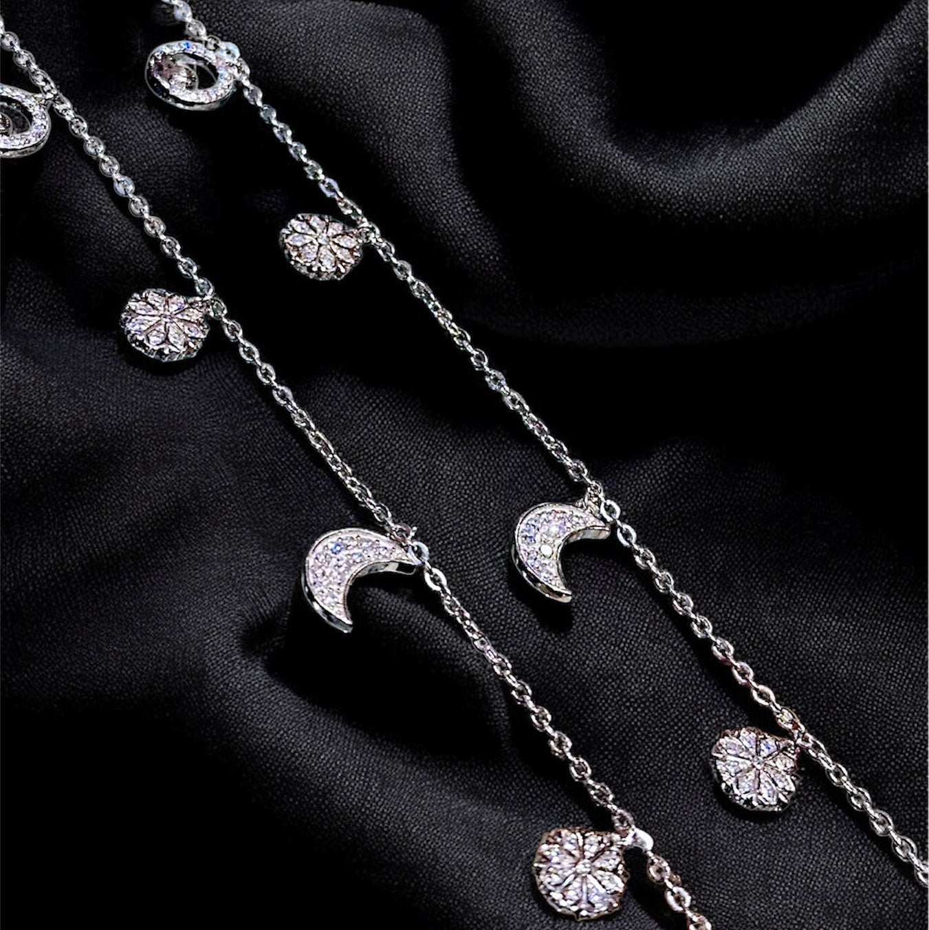 Silver necklace with moon and star pendants on a black fabric background
