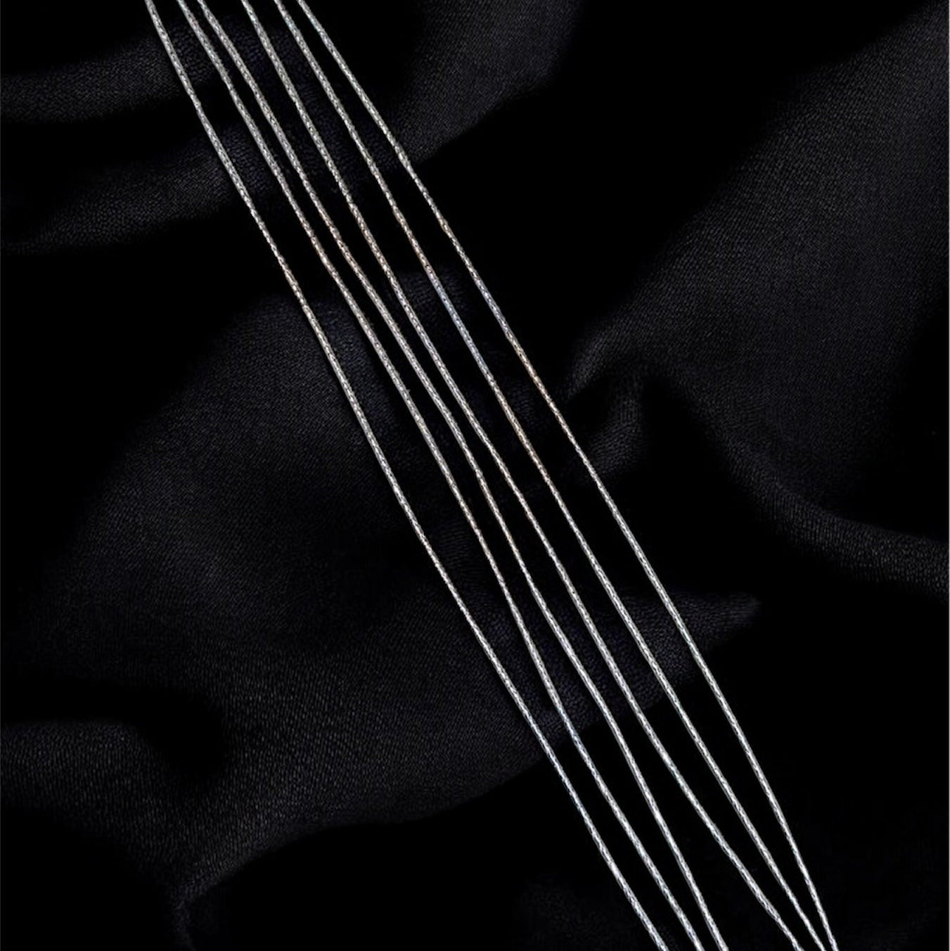 Three silver necklaces on a black fabric background