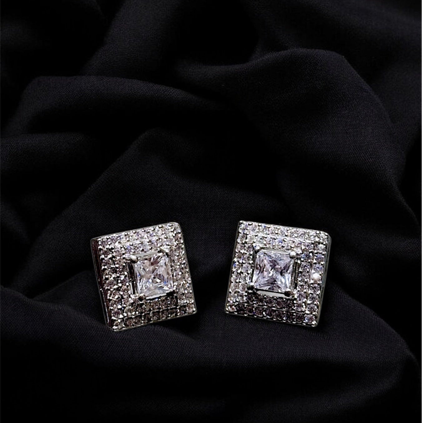 Pair of square-shaped diamond earrings on a black fabric background
