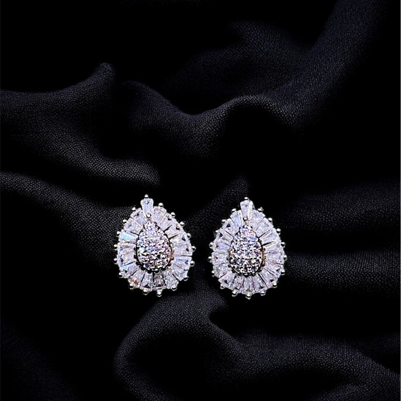 Pair of teardrop-shaped earrings with gemstones on a black fabric background