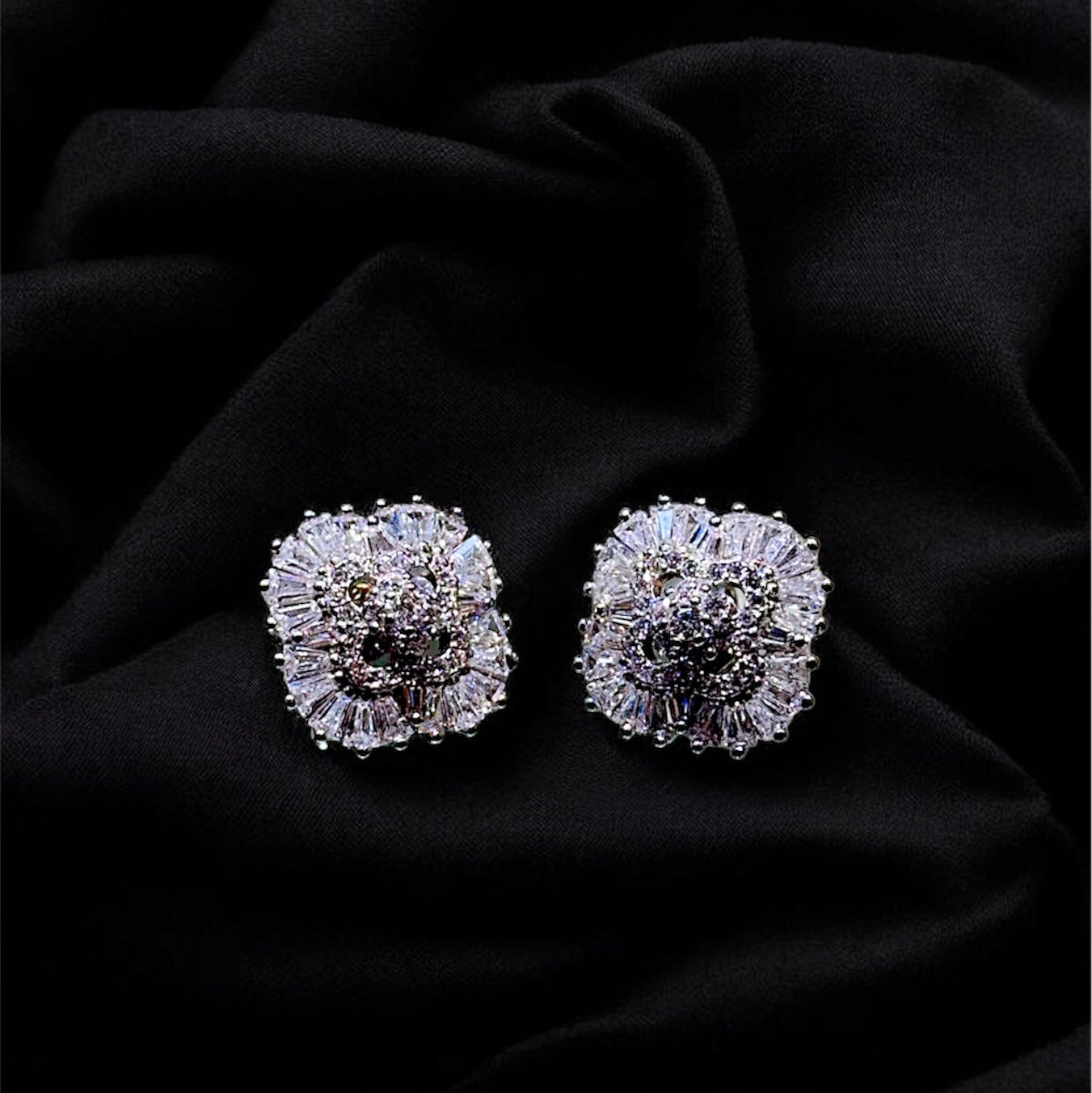 Pair of silver floral earrings on a black fabric background