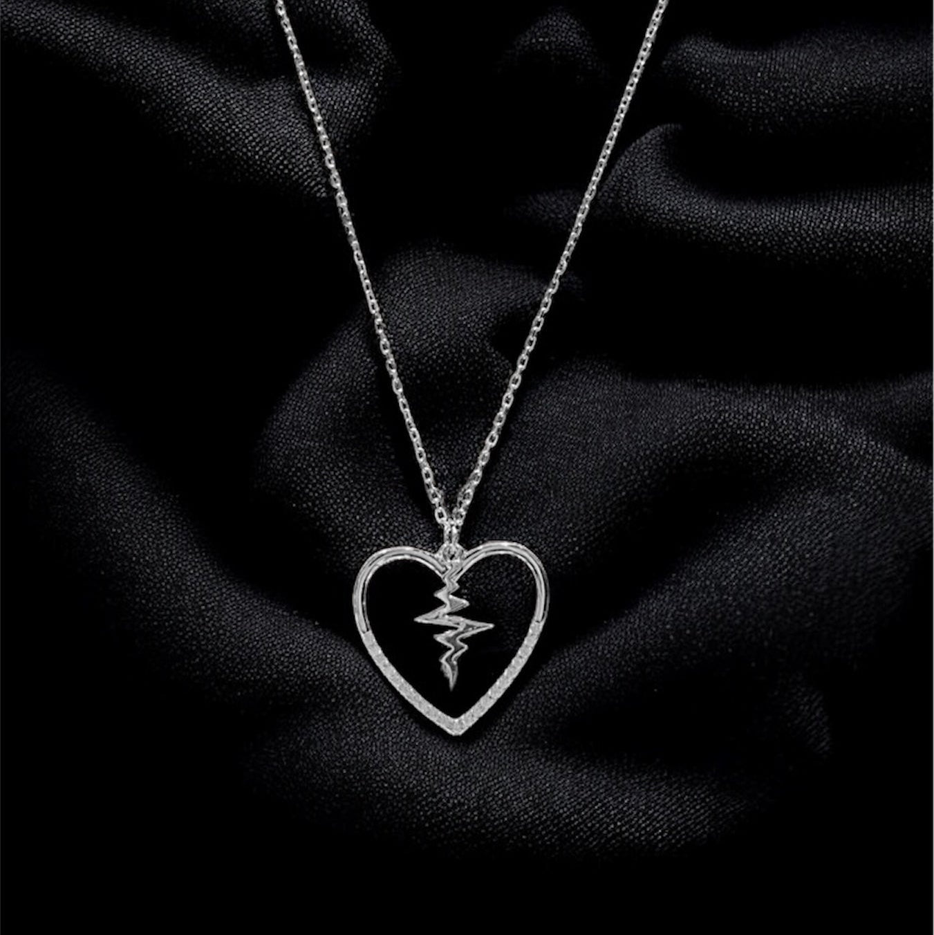 Silver necklace with a heart-shaped pendant on a black fabric background