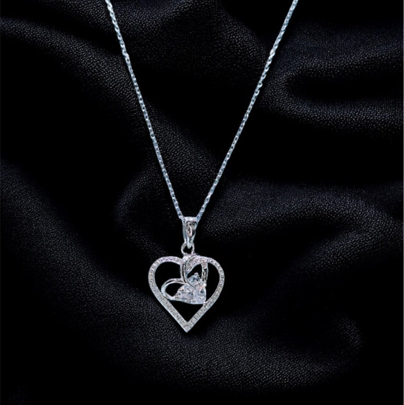 Silver necklace with a heart-shaped pendant on a black fabric background