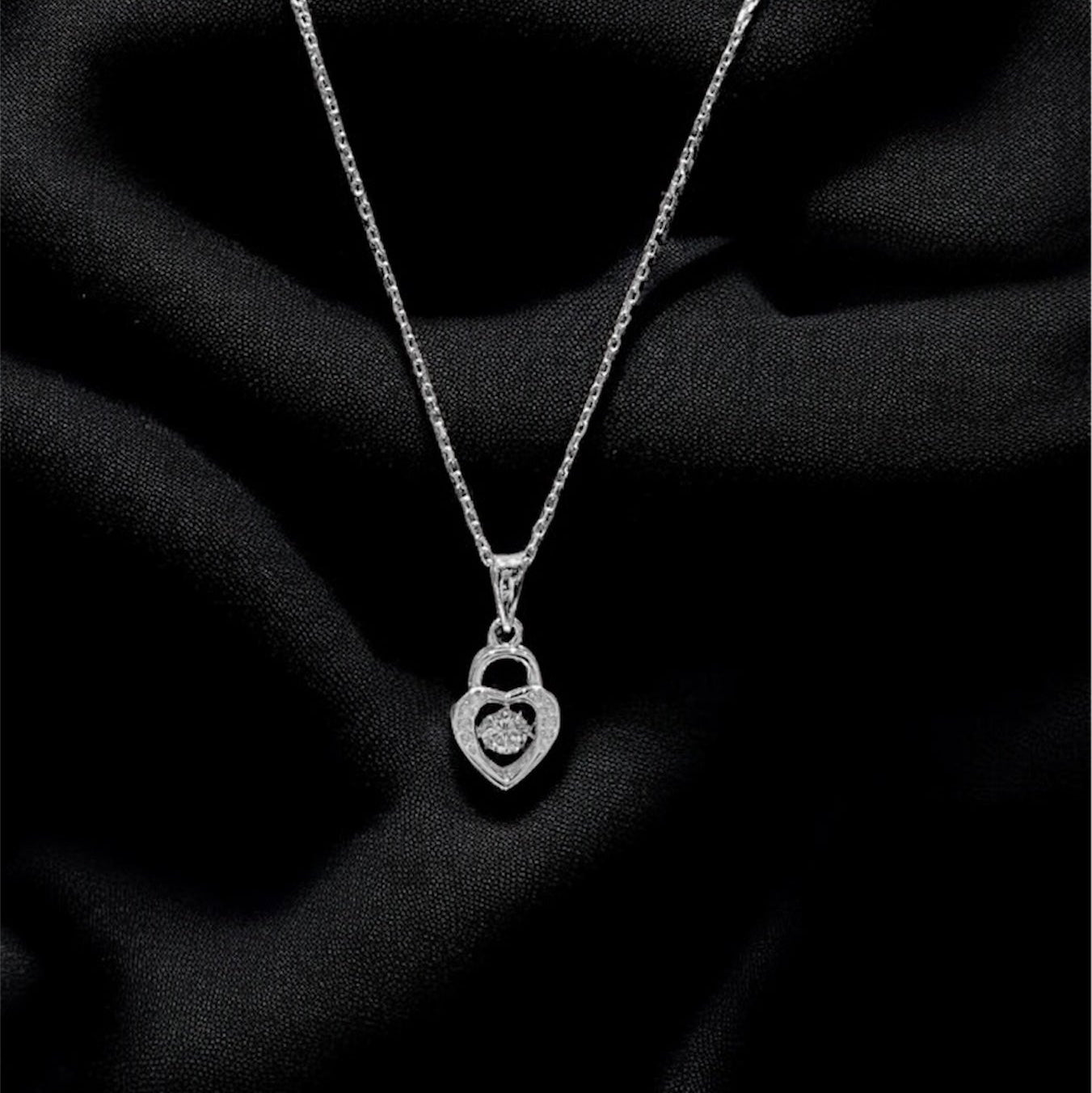 Silver necklace with a heart-shaped pendant on a black fabric background