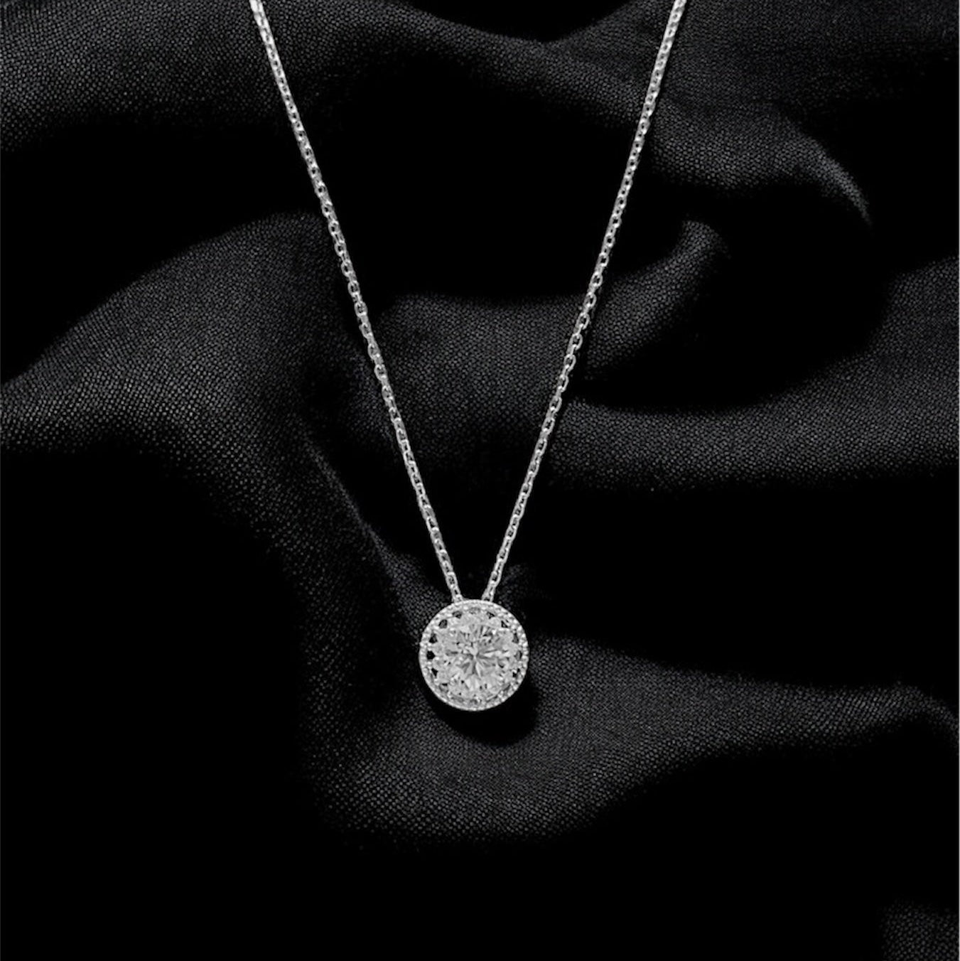 Silver necklace with a round pendant on a black fabric background